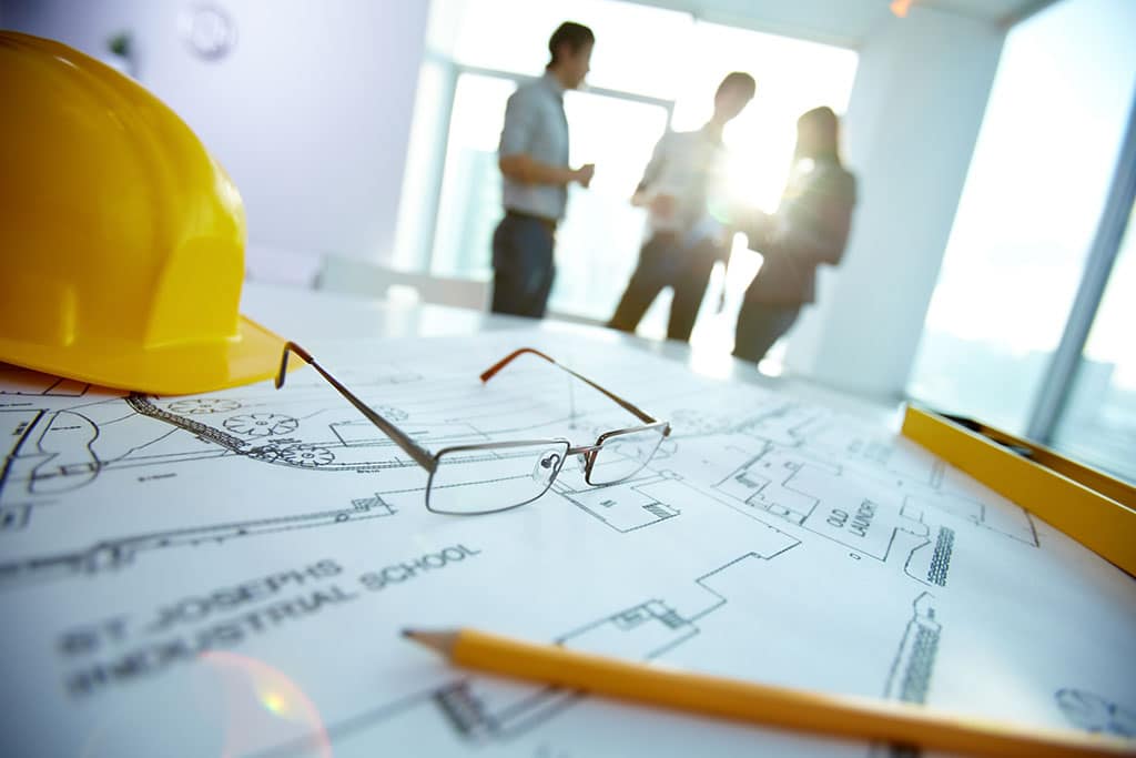 Hard hat sitting on top of plans with Architects in background.